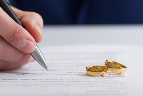 Man signing papers for divorce with his wedding ring next to him