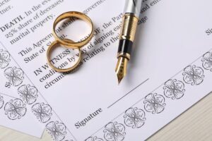 Close-up view of the signature line of a document with a pen and two wedding rings on top of it to symbolize what a prenuptial agreement is.