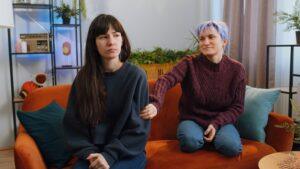 Two women in a lesbian relationship sit unhappily on a couch wondering if lesbians have the highest divorce rate