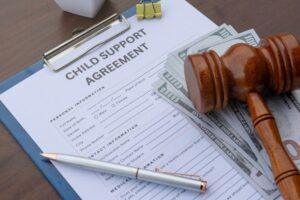 A gavel and dollar bills sit on top of a child support agreement form.
